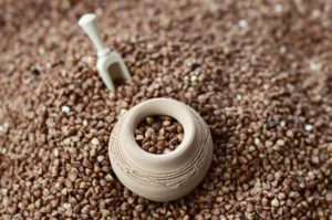 Background image of a large pile of buckwheat, in the middle of which lies a small jug and a wooden spatula for cereals
